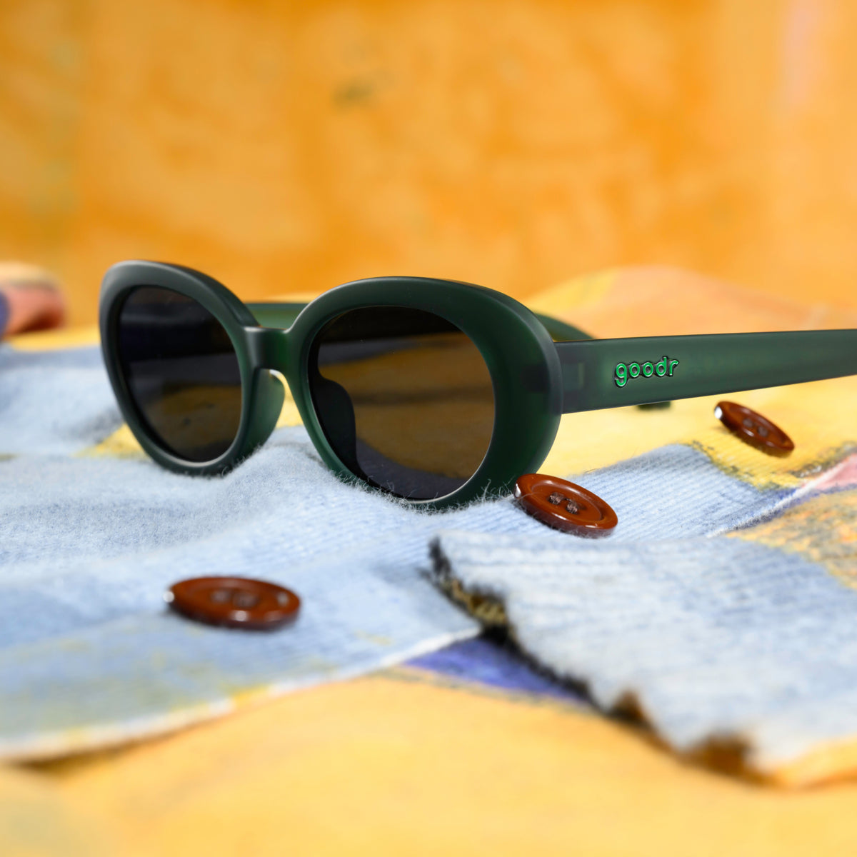 Three-quarter-angle view of a pair of translucent dark green oval sunglasses sitting on a fuzzy, light blue sweater sleeve.