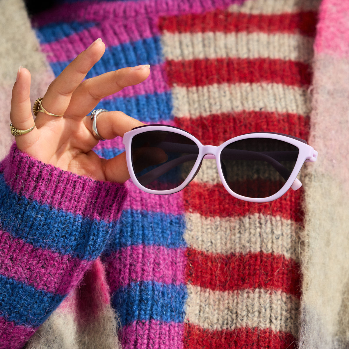 A woman's hand holds a pair of lavender Pounce Gs out in front of her chest. She wears a colorful, fuzzy, striped sweater.
