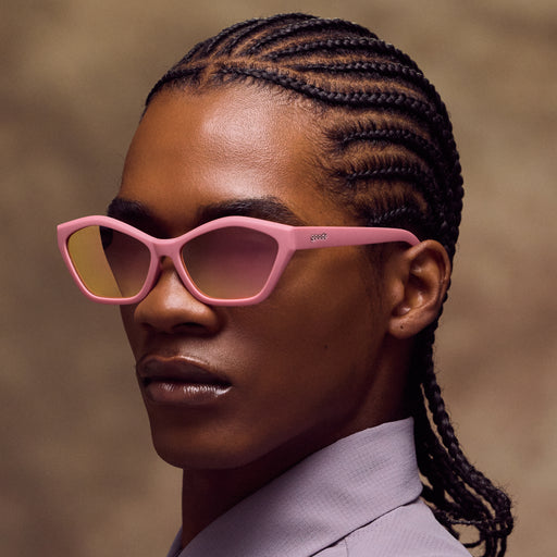 Person wearing pink sunglasses with braided hair against a neutral background