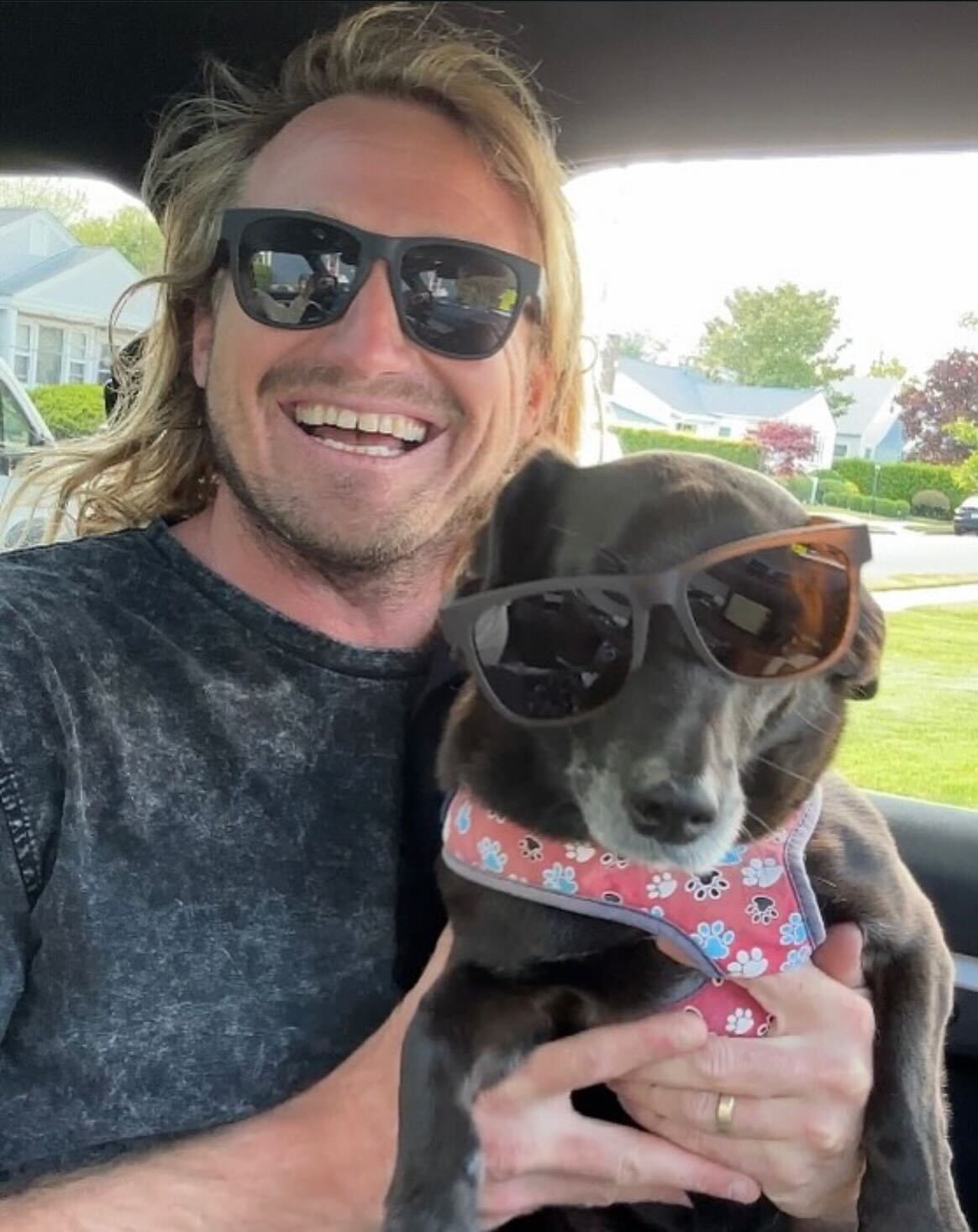 Man holding a dog wearing sunglasses inside a vehicle