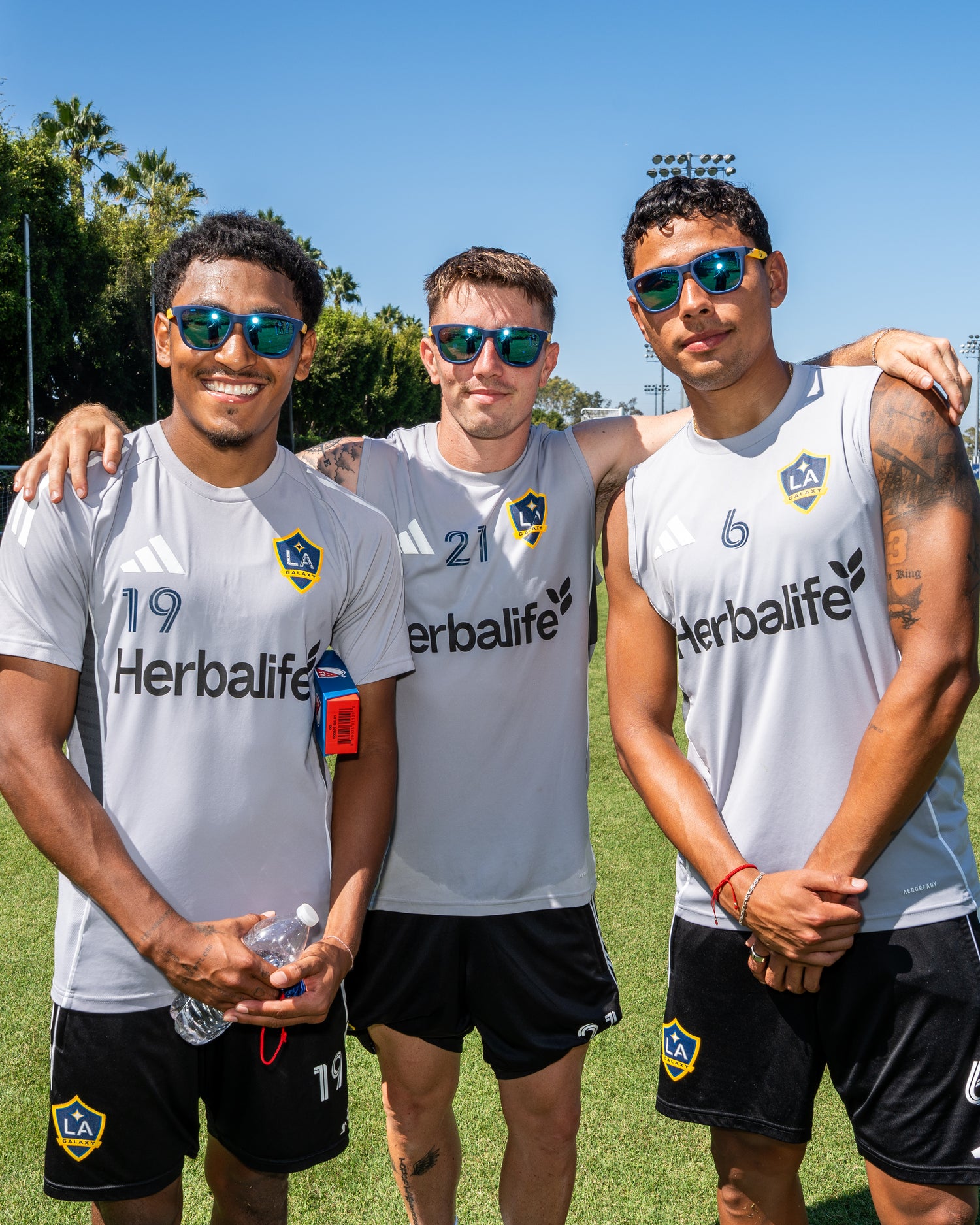 Three men in sports attire with 'La Galaxy' branding on a grassy field.