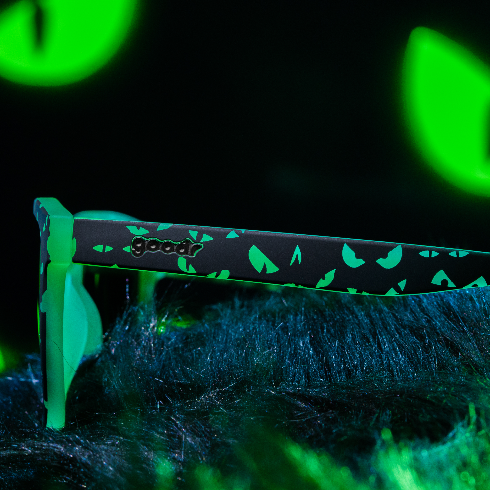 A side close-up of the temple of a pair of spooky, glow-in-the-dark sunnies with a glowing-eyes design is posed on dark fur.