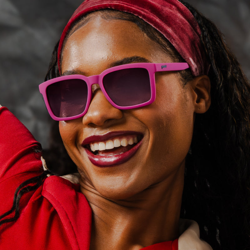 A woman is smiling joyfully in purple sunglasses with a classic square silhouette & purple gradient lenses.