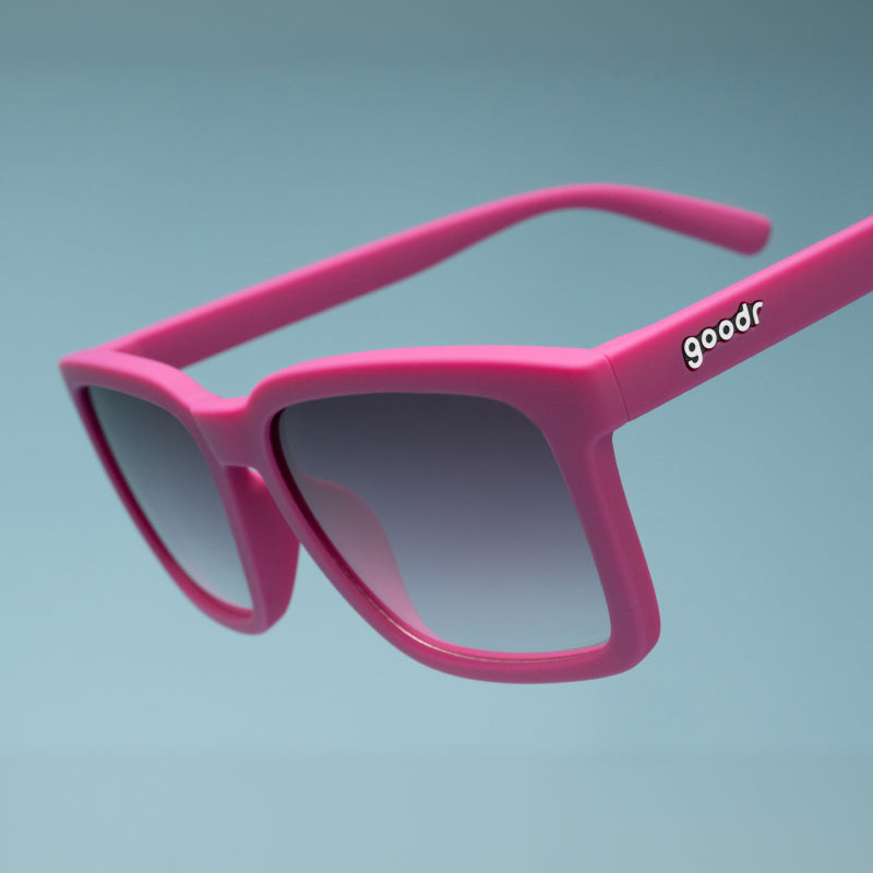 Three-quarter angle close-up view of purple sunglasses with a square silhouette & purple gradient lenses tilted down.