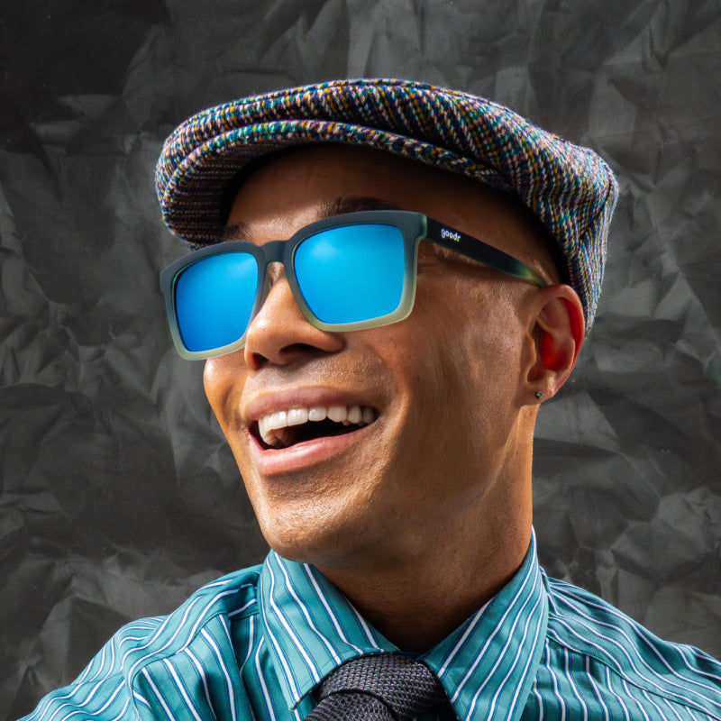 A man is smiling in translucent black & teal square sunglasses w/ blue reflective lenses & a classic square silhouette.