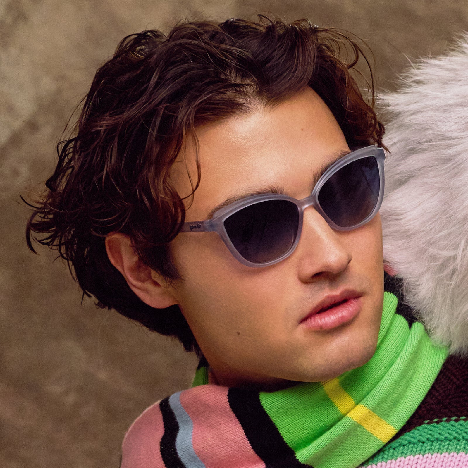 Person wearing sunglasses and a colorful sweater with a neutral background