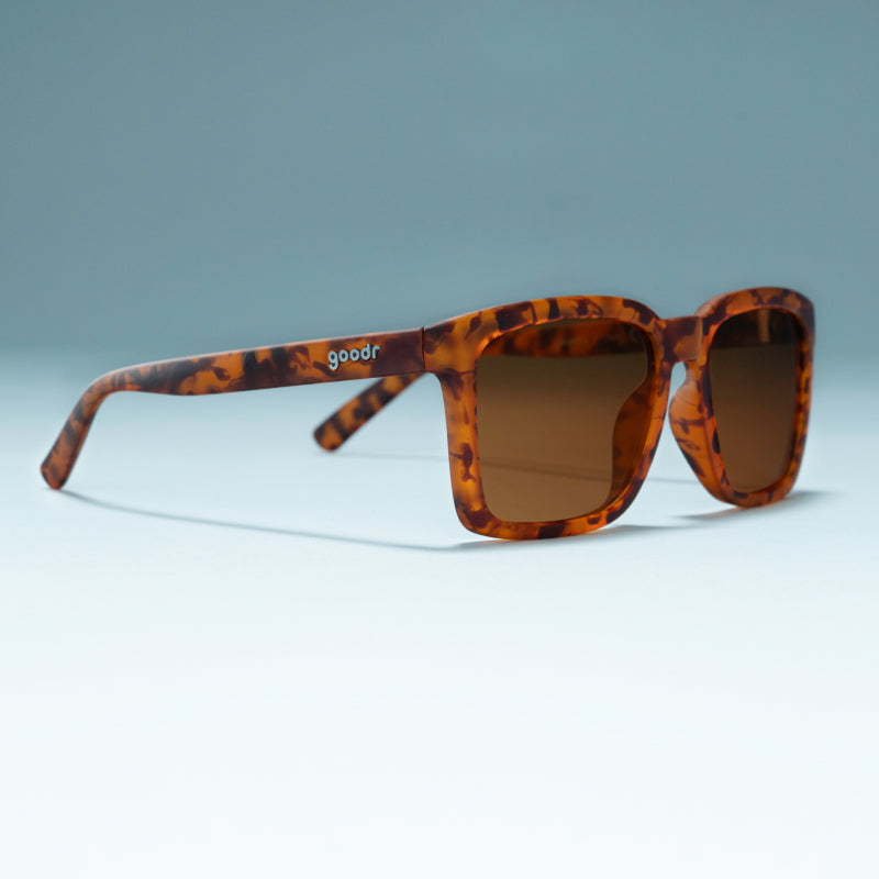 Angled view of translucent brown square shades w/ tortoiseshell pattern & brown nonreflective lenses on a flat surface.