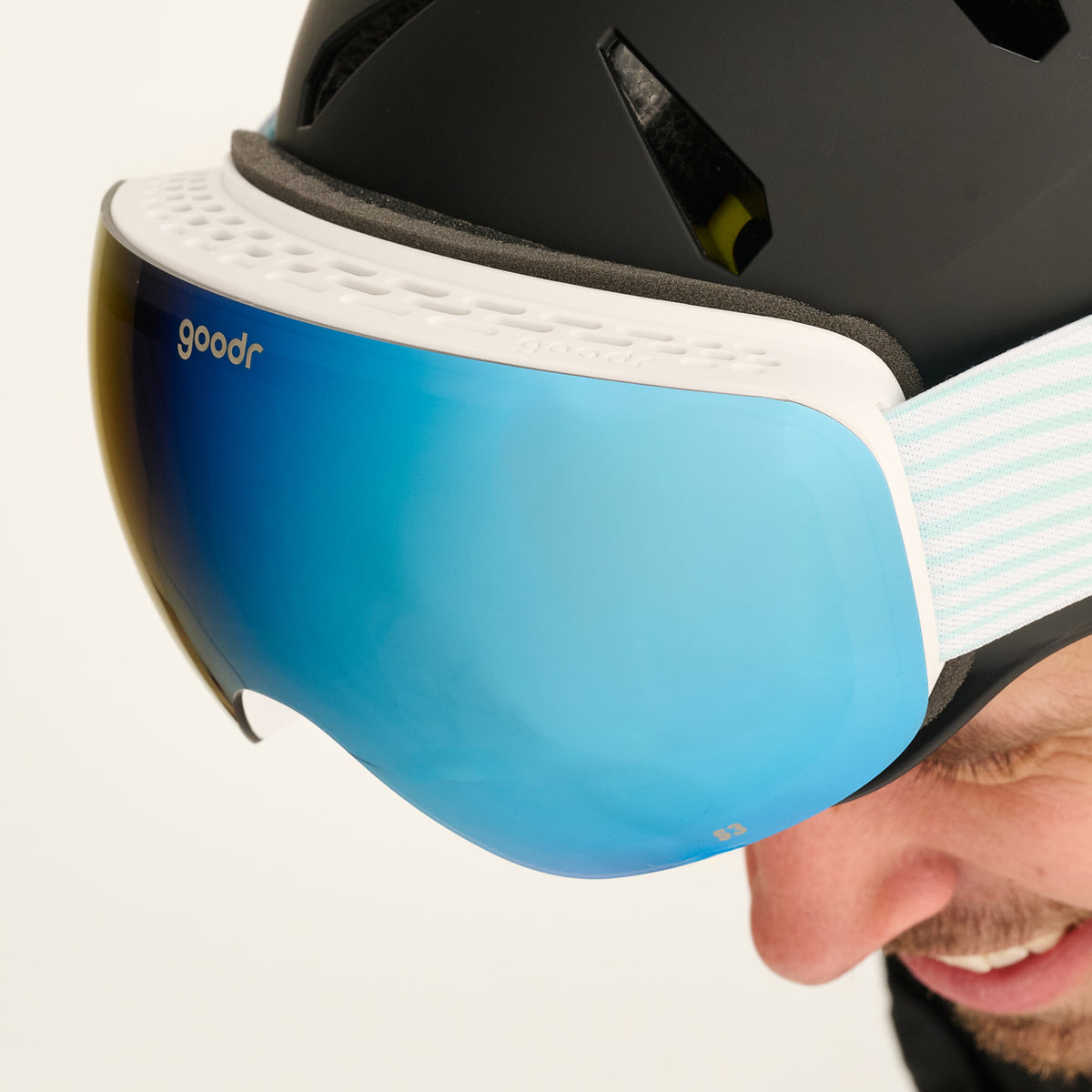Close-up of blue mirrored snow goggles with a white vented frame worn with a black helmet.