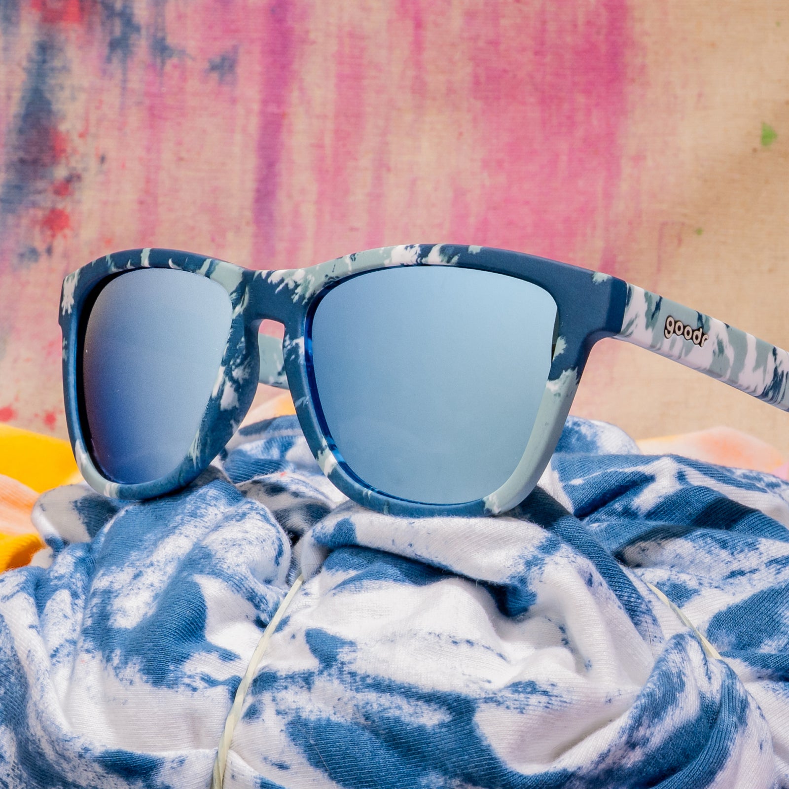 Close-up shot of blue tie-dye sunglasses photographed from behind, sitting on a moody tie-dye fabric backdrop.