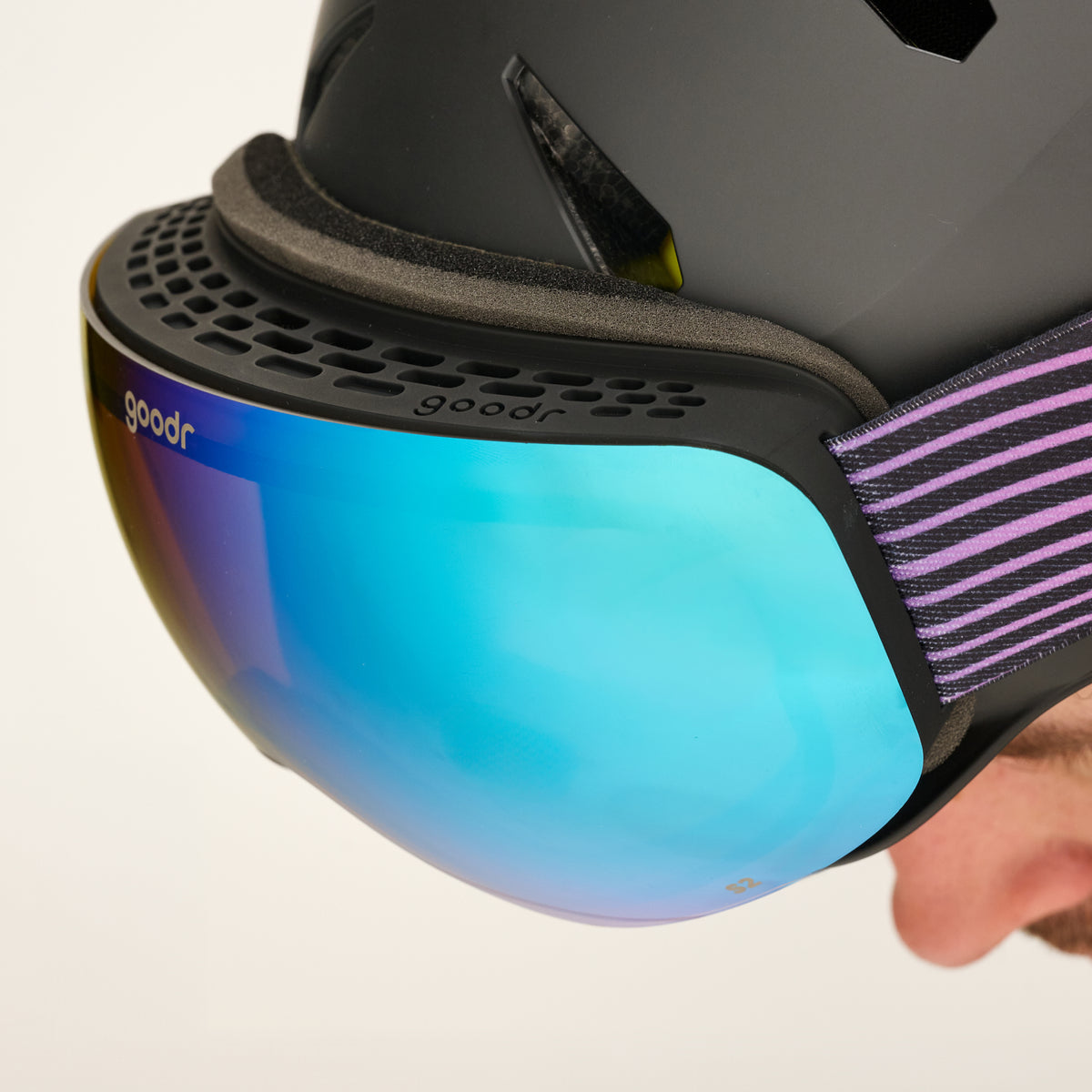 Close-up of bronze blue mirrored snow goggles with a black vented frame worn with a black helmet.