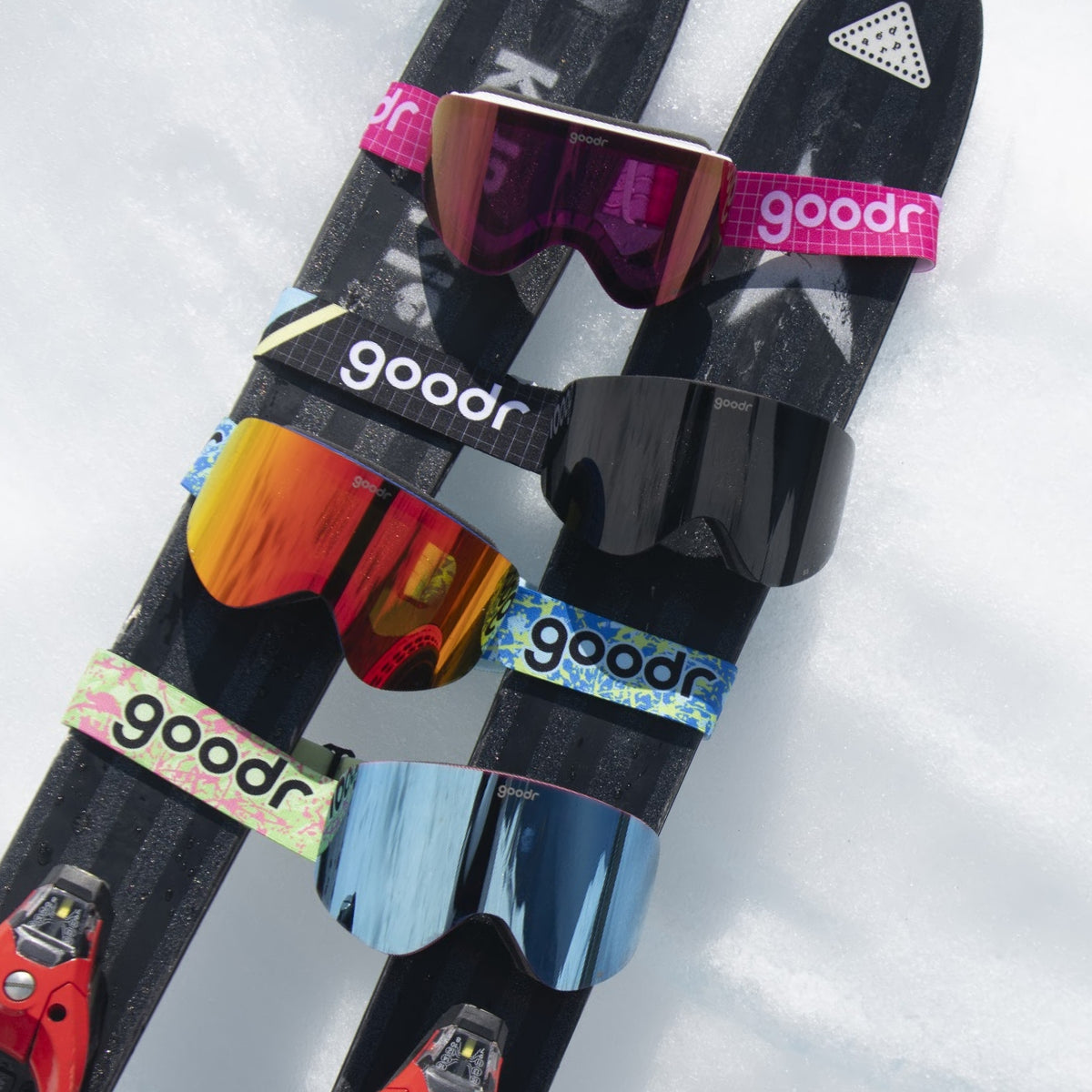 Blue and lime goodr goggle strap shown on ski goggles alongside other colorful goggles on snow.