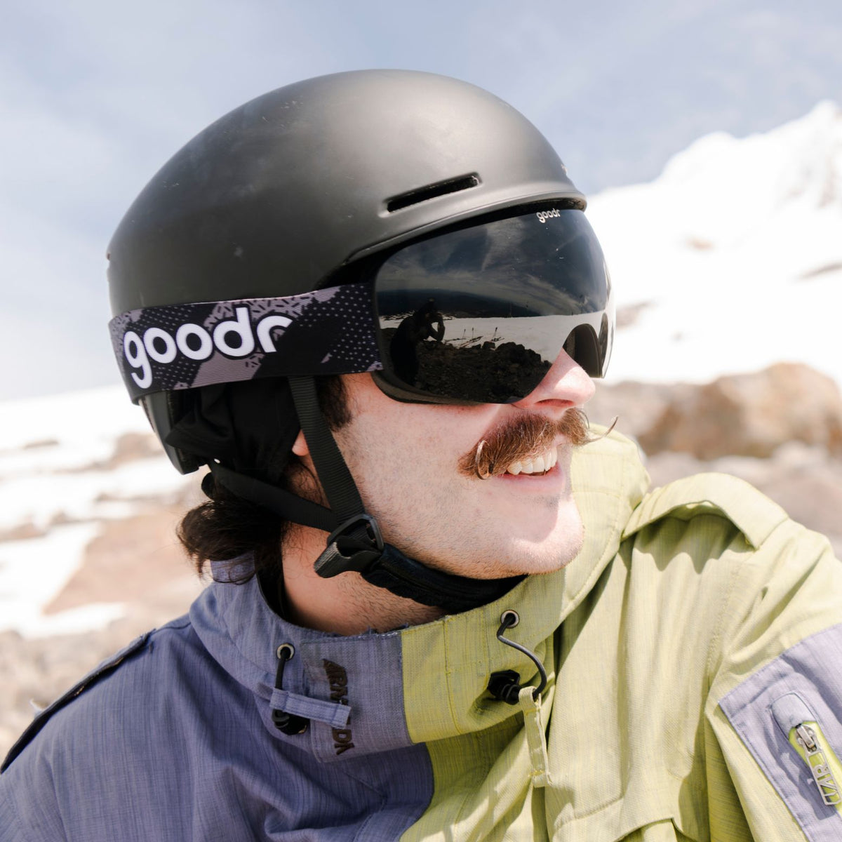 Skier wearing black snow goggles with a patterned goodr strap and black helmet.