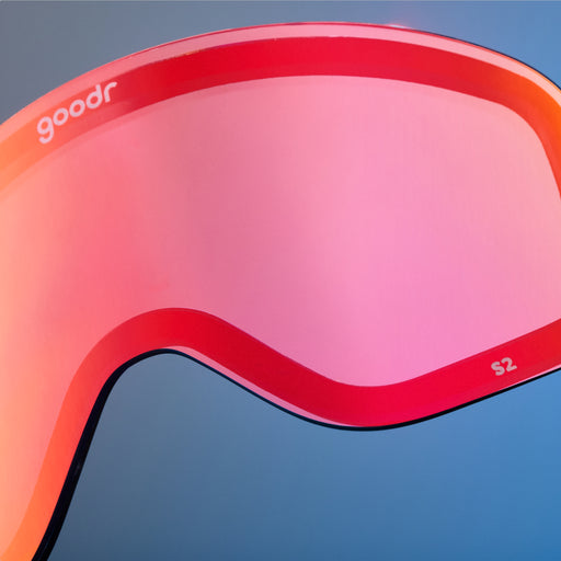 Close-up of red-orange mirrored goodr replacement lens against a blue background.
