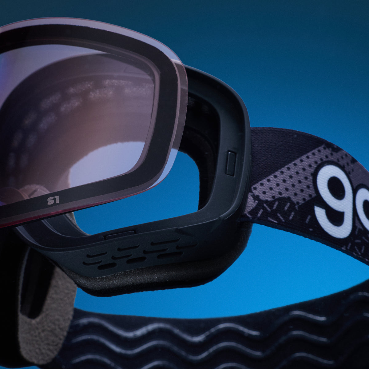 Pale pink replacement lens resting above black goodr ski goggles.