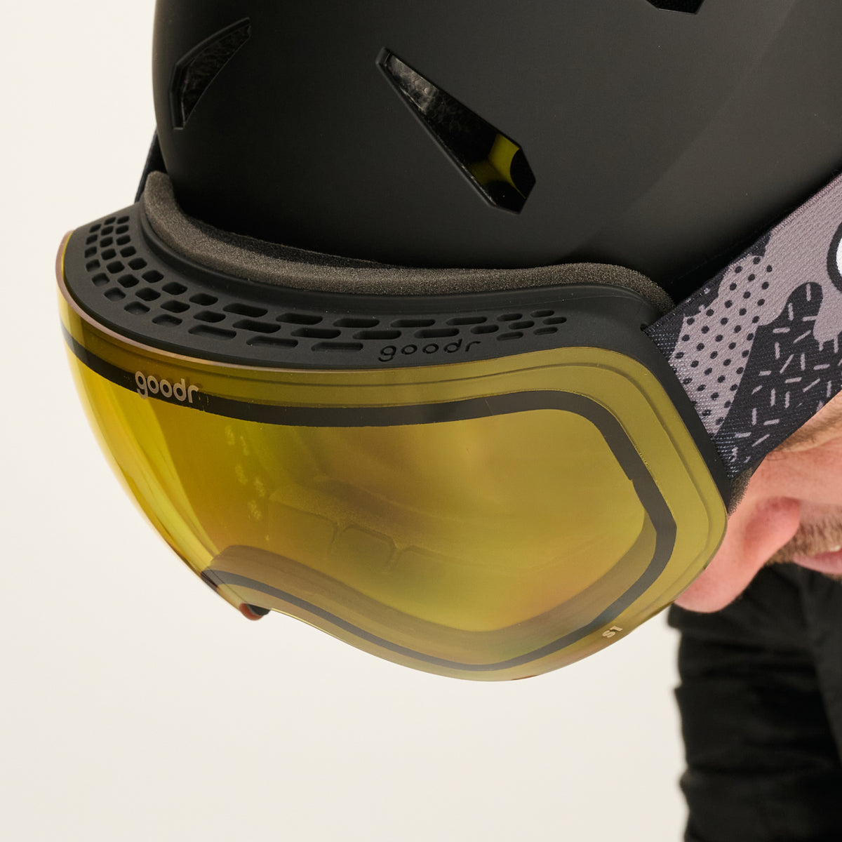 Close-up of yellow snow goggles with a black vented frame worn with a black helmet.
