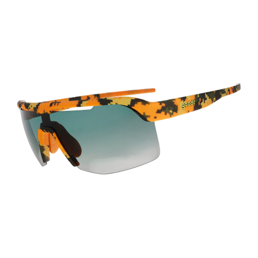 Sport sunglasses with a vibrant orange, yellow, and black camouflage pattern on the frame and arms, featuring a green-to-gray gradient lens and a small green 'goodr' text logo on the temple.