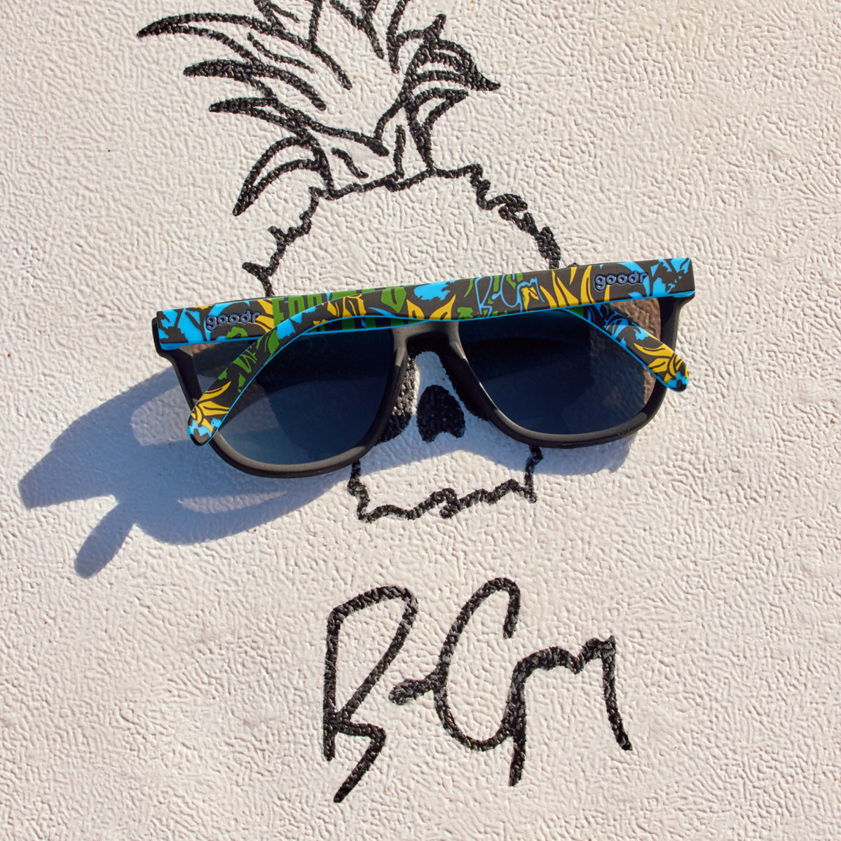 A folded pair of goodr sunglasses on top of Ben Gravy’s iconic pineapple logo and personal signature.