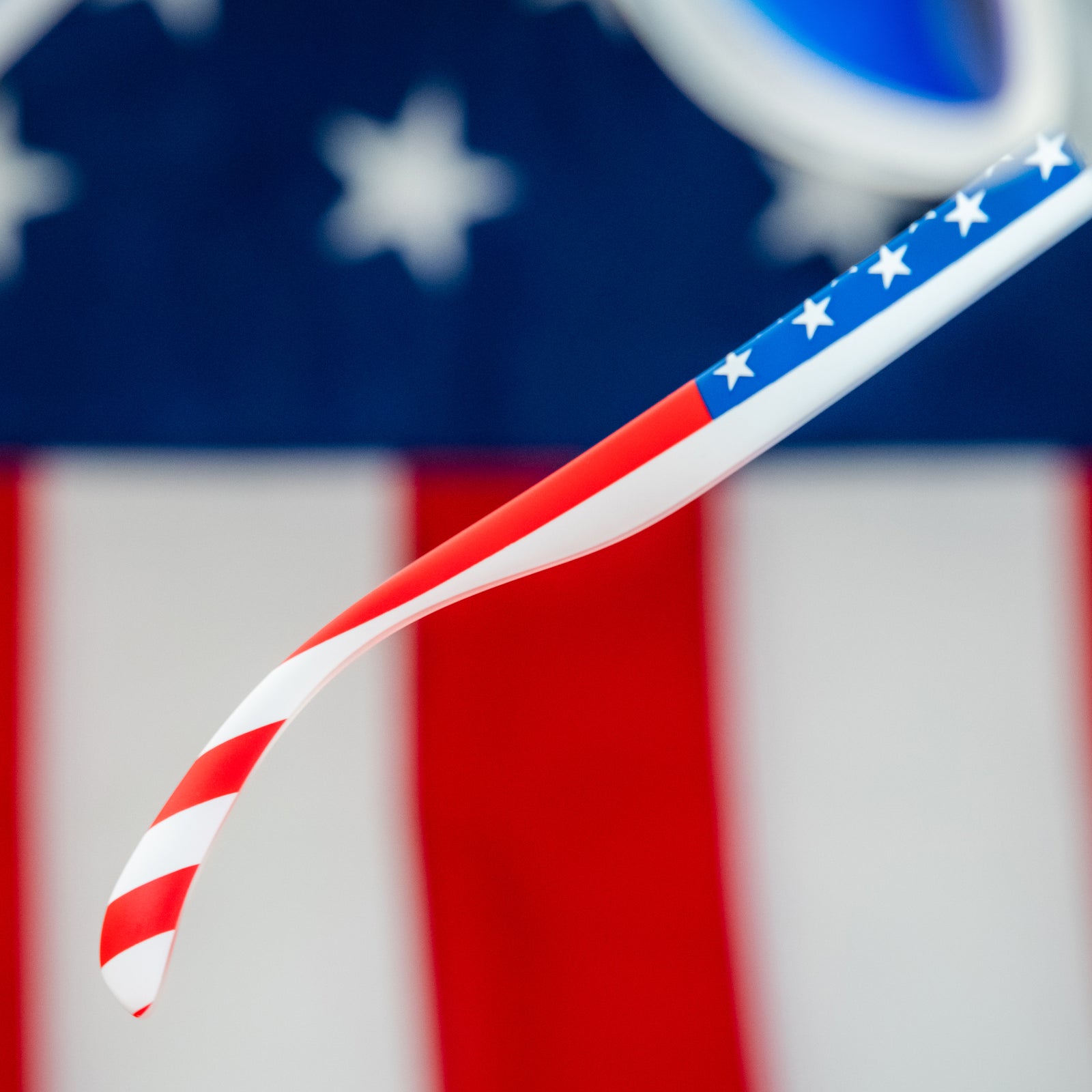 Angled view of clear shades w/ an American flag pattern+blue reflective lenses on a stylized background.