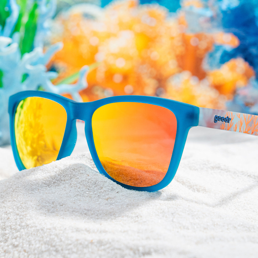 Blue goodr sunglasses with orange lenses and a coral design on the temples