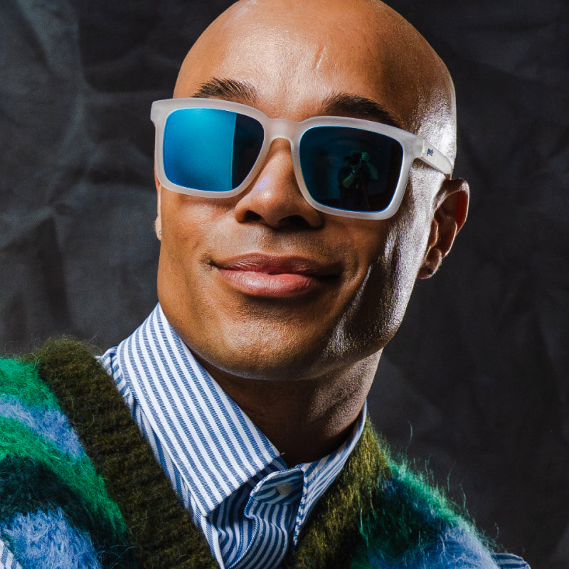 A man smiling joyfully in translucent clear sunglasses with a square silhouette and light blue reflective lenses.