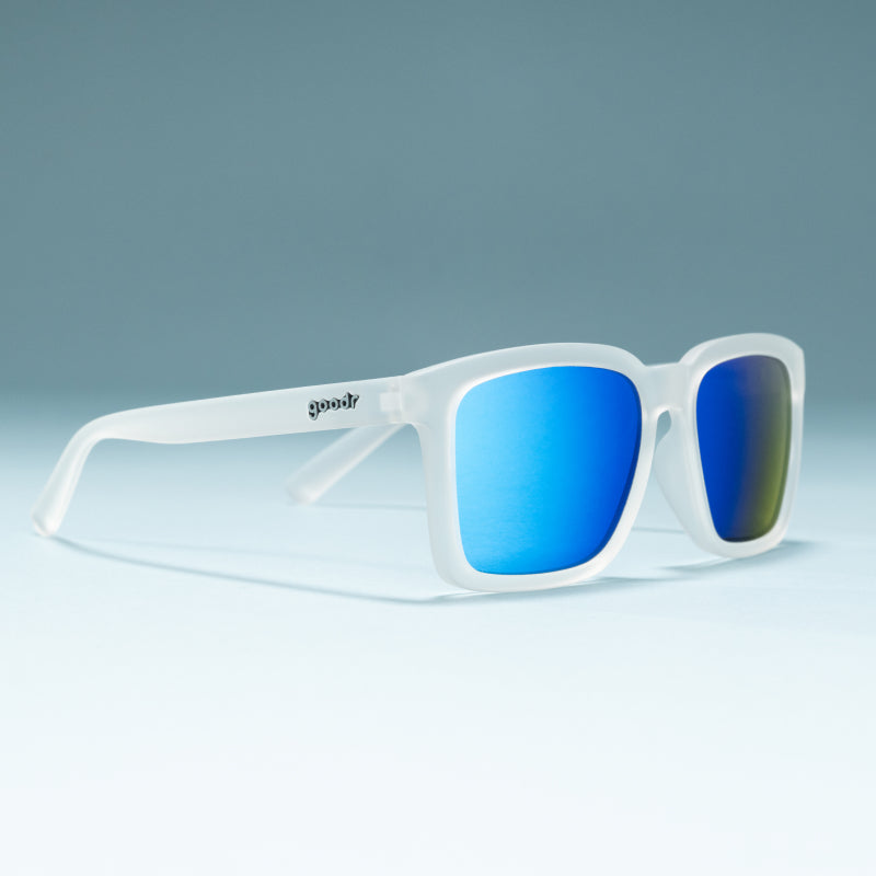 Three-quarter angle view of translucent clear shades w/ a square silhouette & blue reflective lenses on a flat surface.