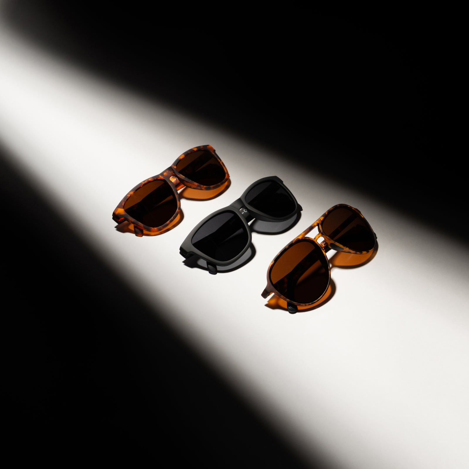 Three pairs of sunglasses on a white surface with a black background