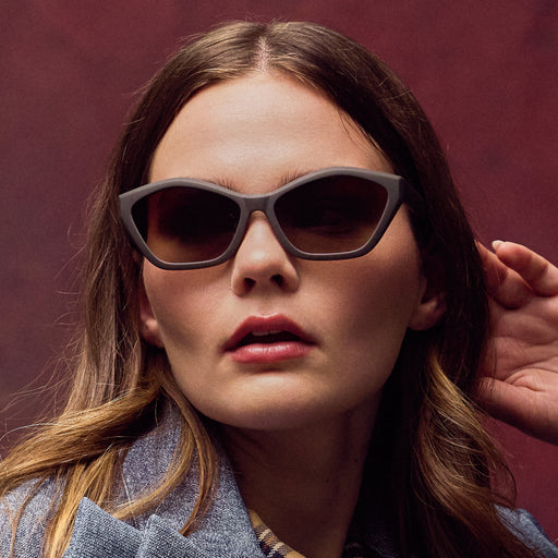 Woman wearing dark sunglasses against a maroon background