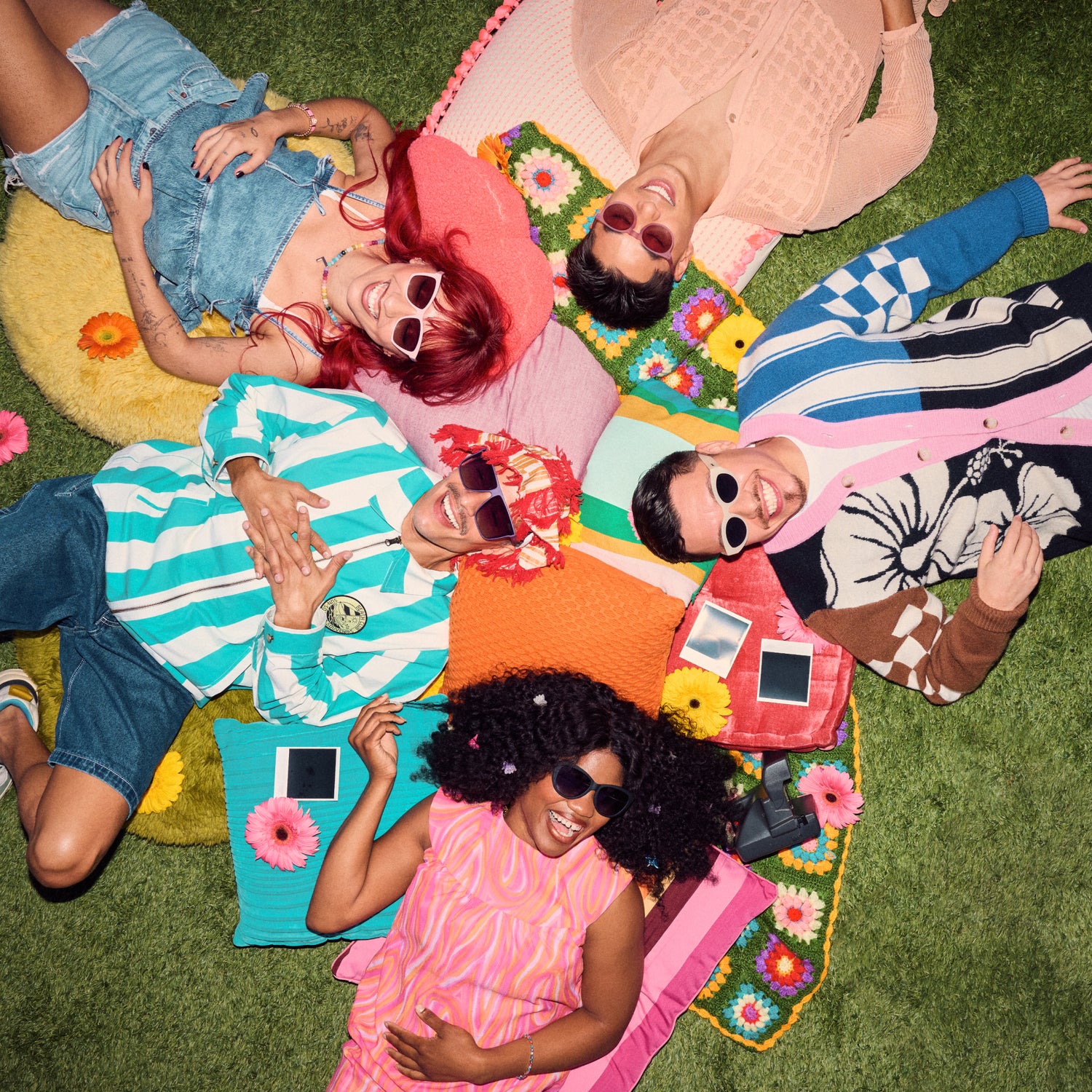 Five people lying on a colorful blanket on grass, smiling and posing.